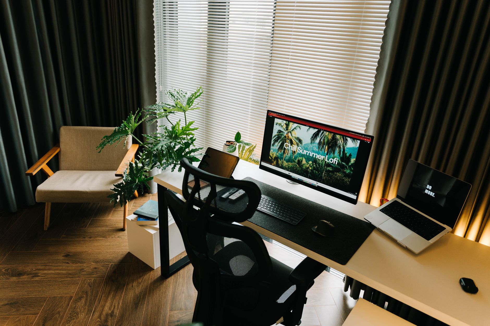A stylish home office setup with a computer, laptop, and indoor plants by a window.