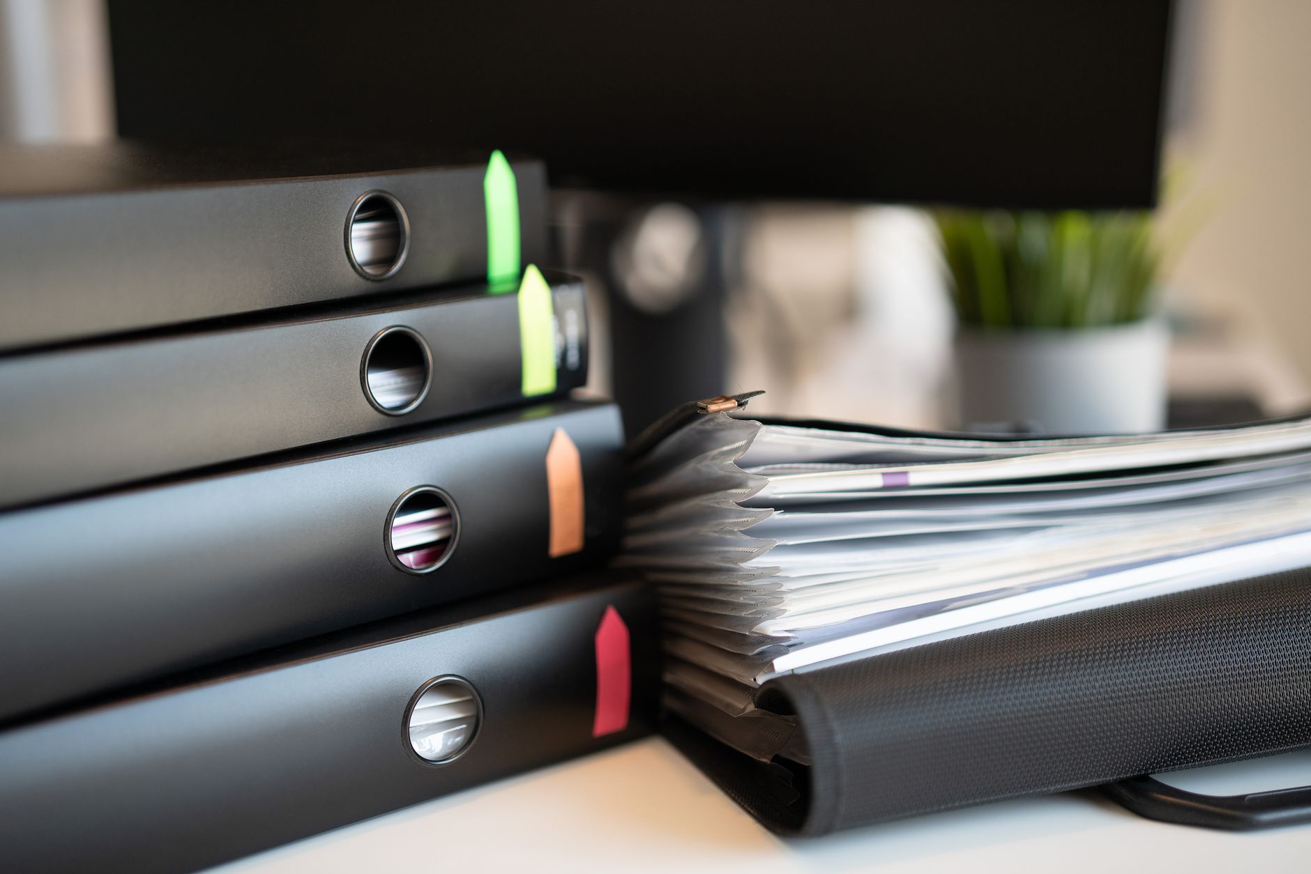 Stack of colorful ring binders and documents on a modern office desk setting.
