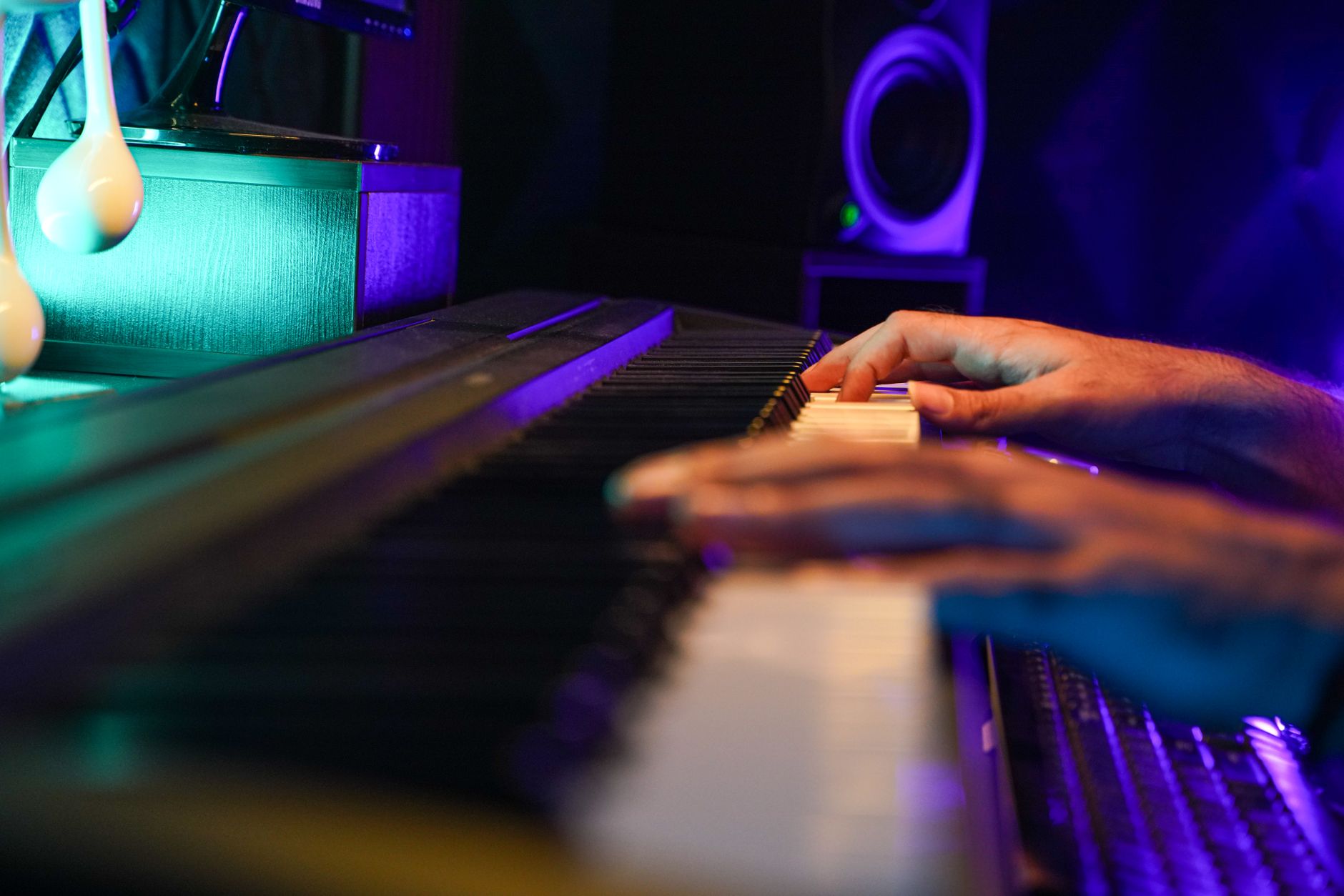 Hands playing a keyboard in a vibrant music studio with colorful lighting.