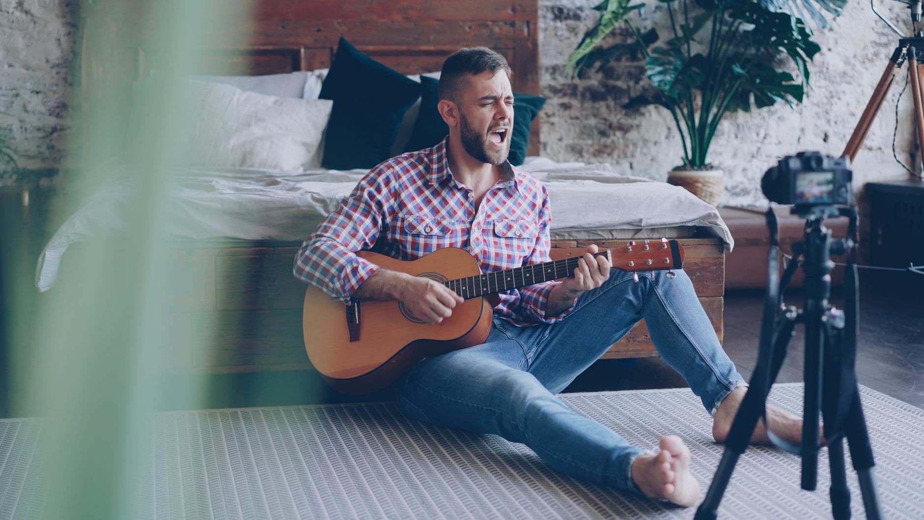 Man playing guitar sitting on the floor, recording a video at home.