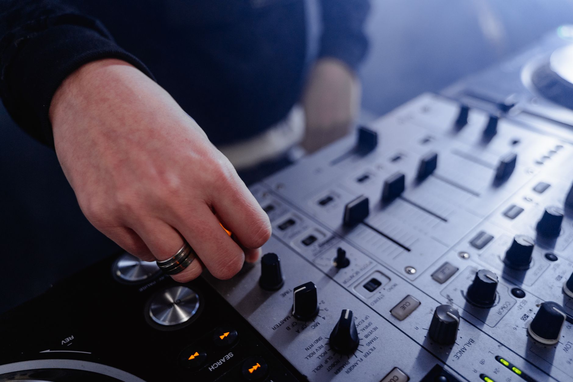 Hand adjusting controls on a DJ mixer at an indoor music event.