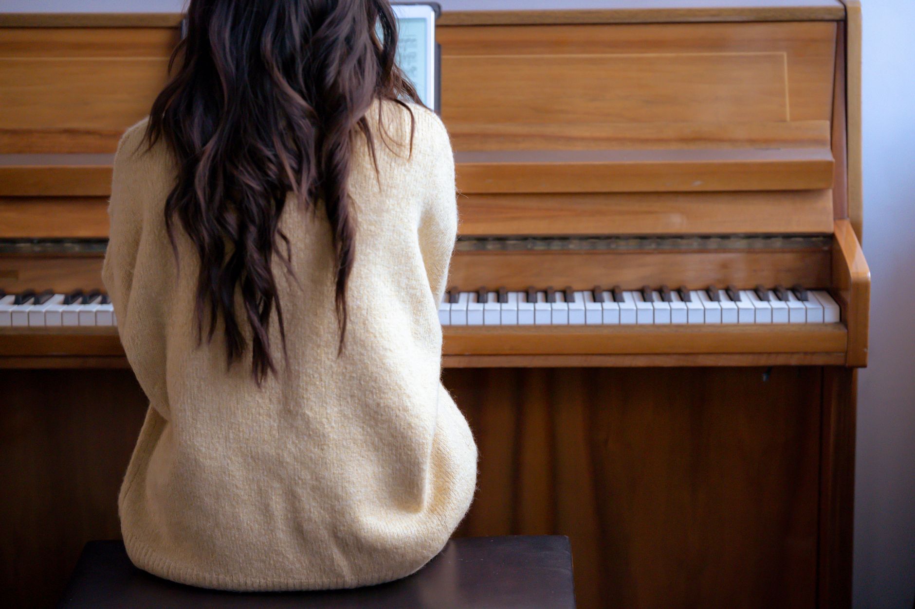 Back view of crop faceless female musician playing piano and using tablet for practicing skills